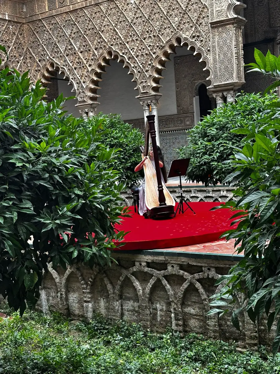 Actuación de arpa sobre una tarima roja en un patio del Real Alcázar.
