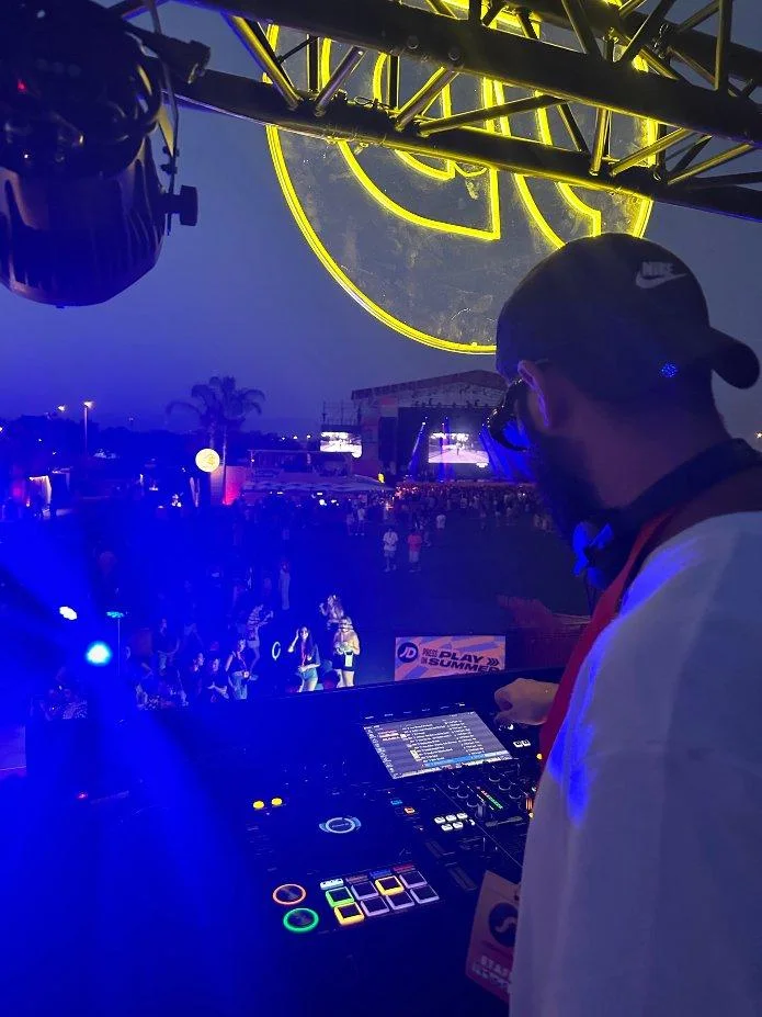 El DJ del JD Corner pinchando de noche frente al logo de neón y el público.