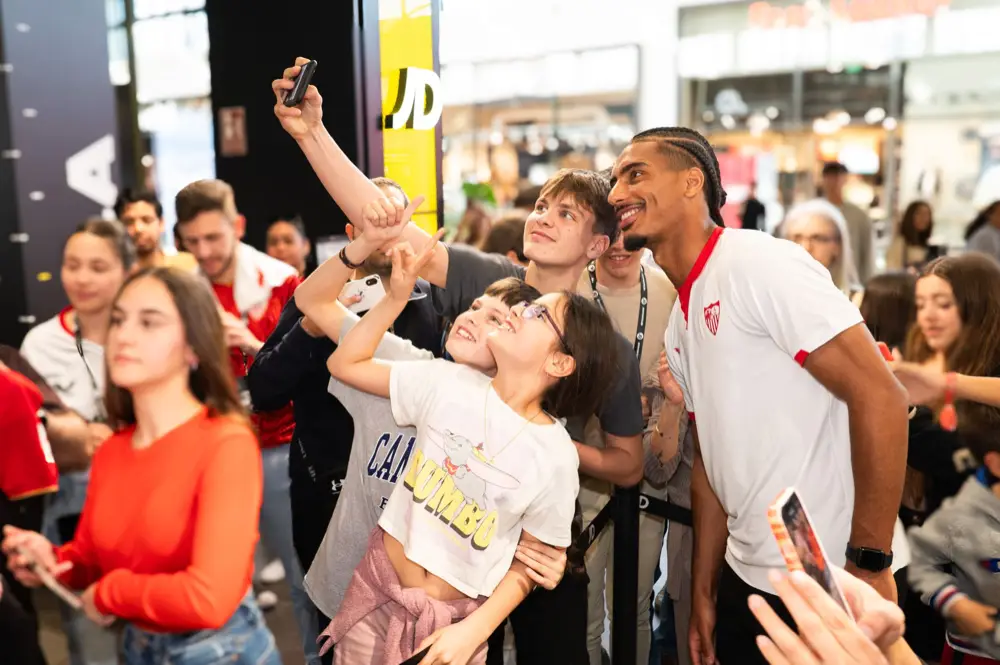 Aficionados haciéndose selfies con un jugador del Sevilla FC dentro de la tienda JD.