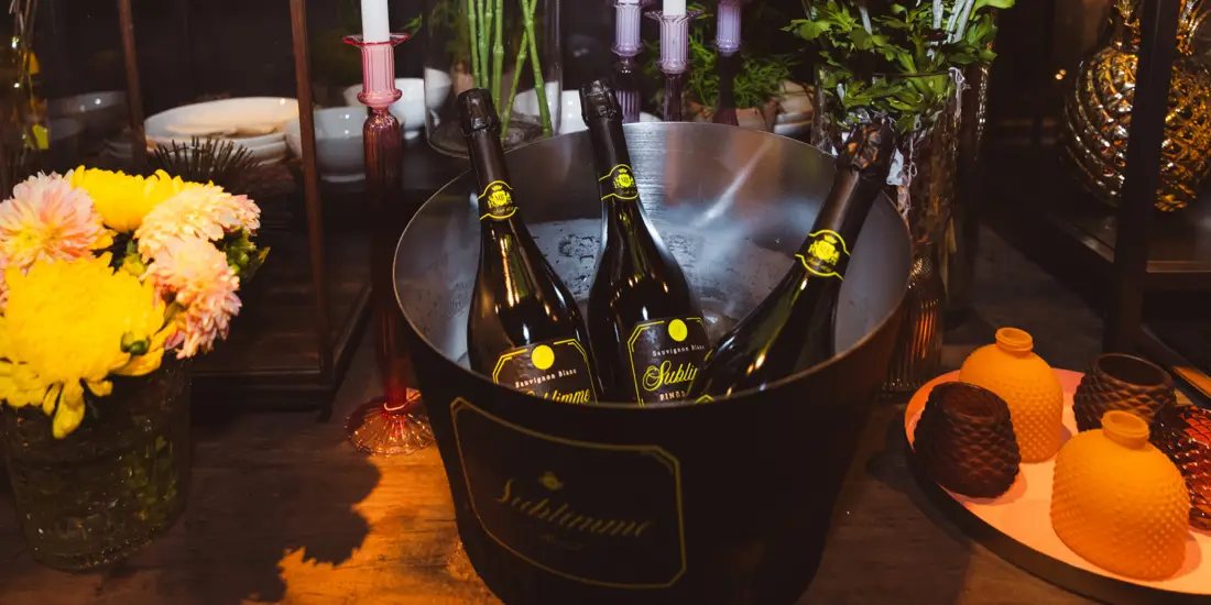 Cubitera con botellas de Sublimme rodeada de composiciones florales.